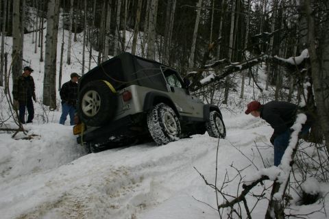 2003 Jeep TJ - A silver 2003 Jeep TJ is stuck in a snowy wooded area with three people nearby.