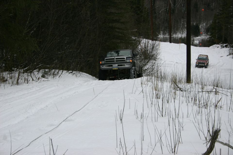 Dark pickup truck and red SUV on a snowy trail, trees in background