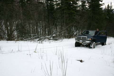2003 Jeep TJ - A blue pickup truck is parked in a snowy field with trees behind it. A tow rope is visible.