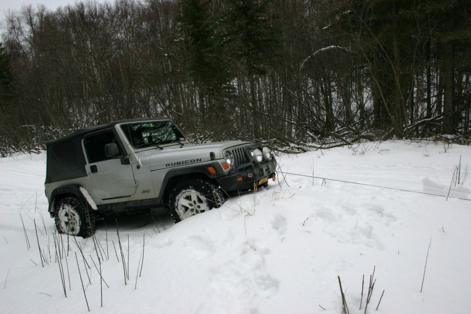 Silver Jeep Wrangler TJ stuck in snow, with a tow rope attached to the front bumper