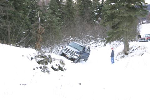 2003 Jeep TJ - A dark blue pickup truck is stuck in a snowy ditch, with another vehicle visible in the background.