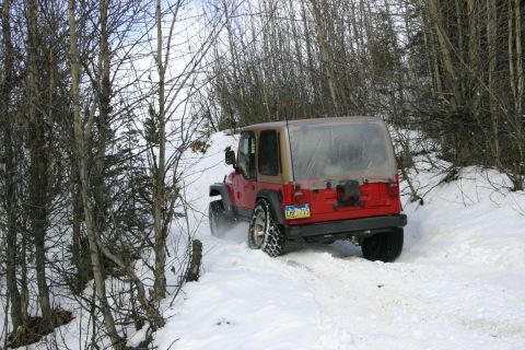 2003 Jeep TJ - A red Jeep Wrangler navigates a snow-covered path through a wooded area.