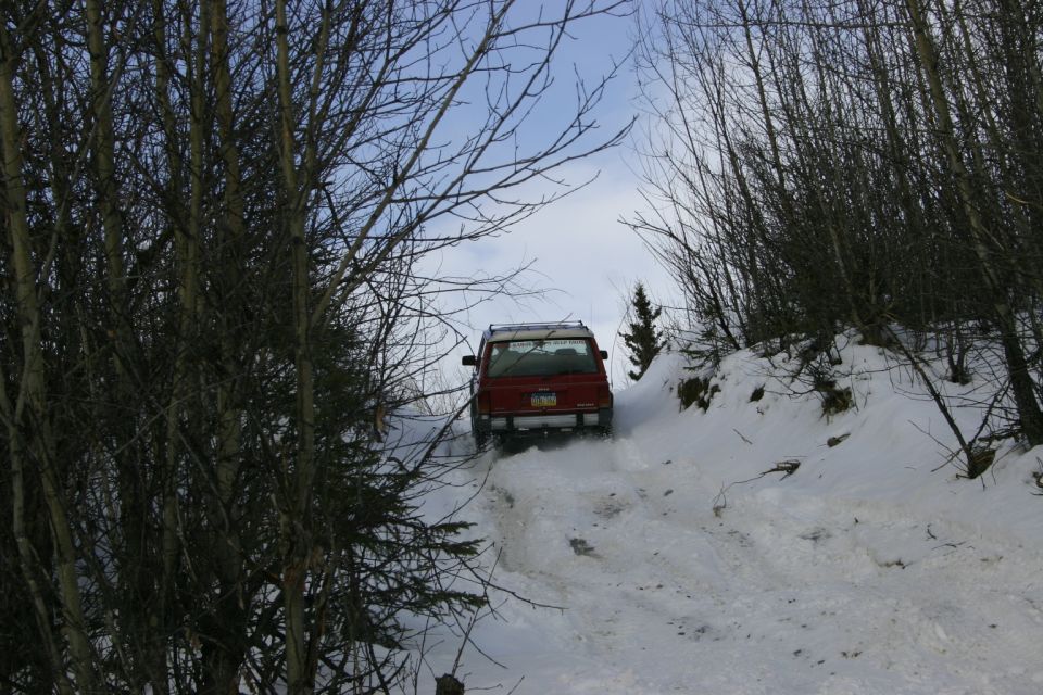 Red 2003 Jeep TJ driving up a snowy, wooded trail