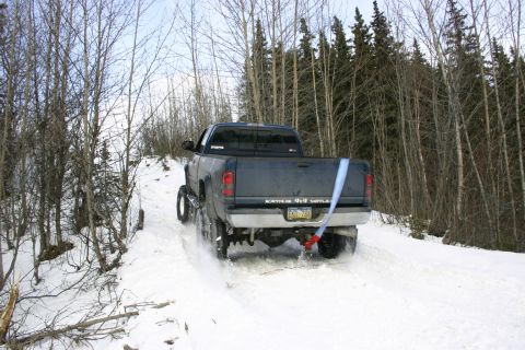 2003 Jeep TJ - Pickup truck navigates a snowy path in a wooded area, kicking up snow from its tires.