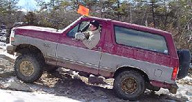 1995 Ford Bronco - A two-tone Ford Bronco navigates a challenging off-road course with a driver behind the wheel.