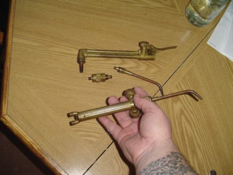 1993 Ford Bronco - A hand holds a welding torch with a cutting attachment, next to another torch head on a table.