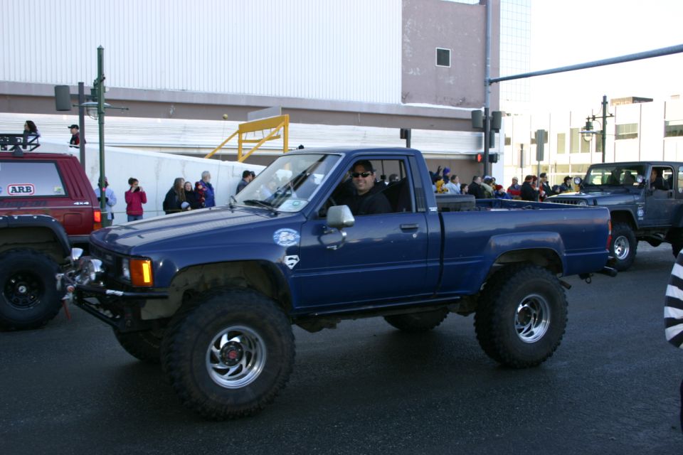 Blue pickup truck with lifted suspension and large tires, seen from the front-left