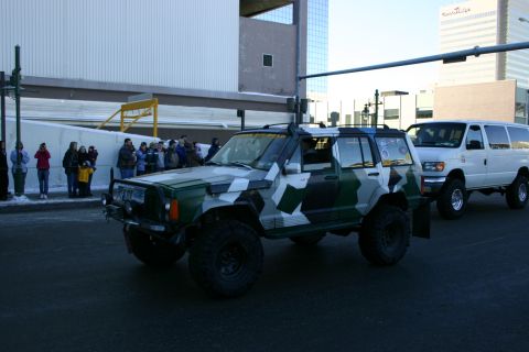 2003 Jeep TJ - A modified Jeep Cherokee XJ and a Ford van drive down a city street during a parade.