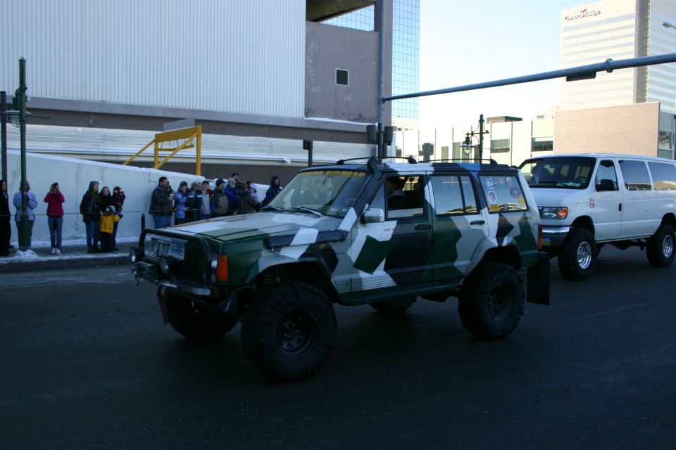 Camouflage-wrapped Jeep Cherokee XJ with lifted suspension and off-road tires, followed by a white Ford Econoline van