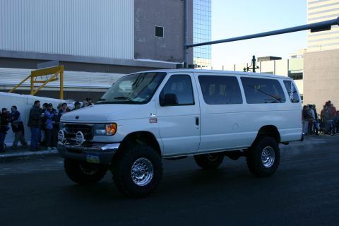 2003 Jeep TJ - A lifted van with large tires is parked on a street, with onlookers in the background.