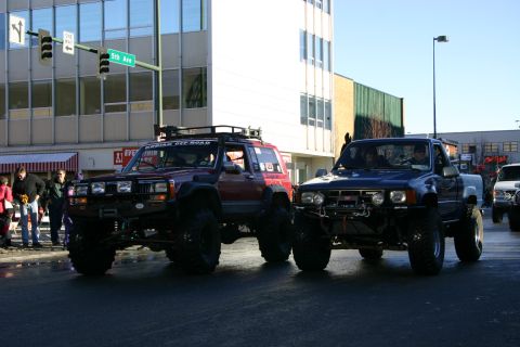 2003 Jeep TJ - Two heavily modified off-road vehicles participate in a parade on a city street.