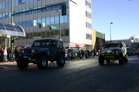 2003 Jeep TJ - Several modified off-road vehicles participate in a street parade, with spectators lining the route.