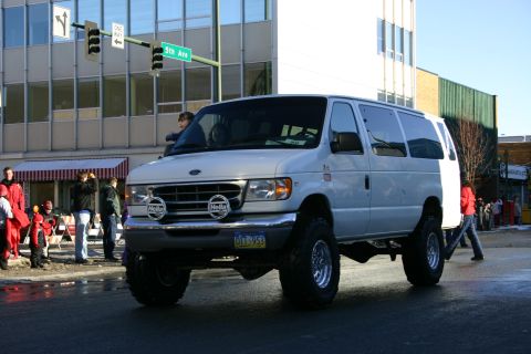 2003 Jeep TJ - This lifted Ford E-Series van is participating in a parade on a city street.