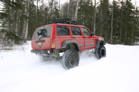 2003 Jeep TJ - A red Jeep Cherokee XJ navigates a snowy path through a wooded area.