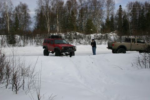 2003 Jeep TJ - Two trucks are parked on a snow-covered road with trees in the background.