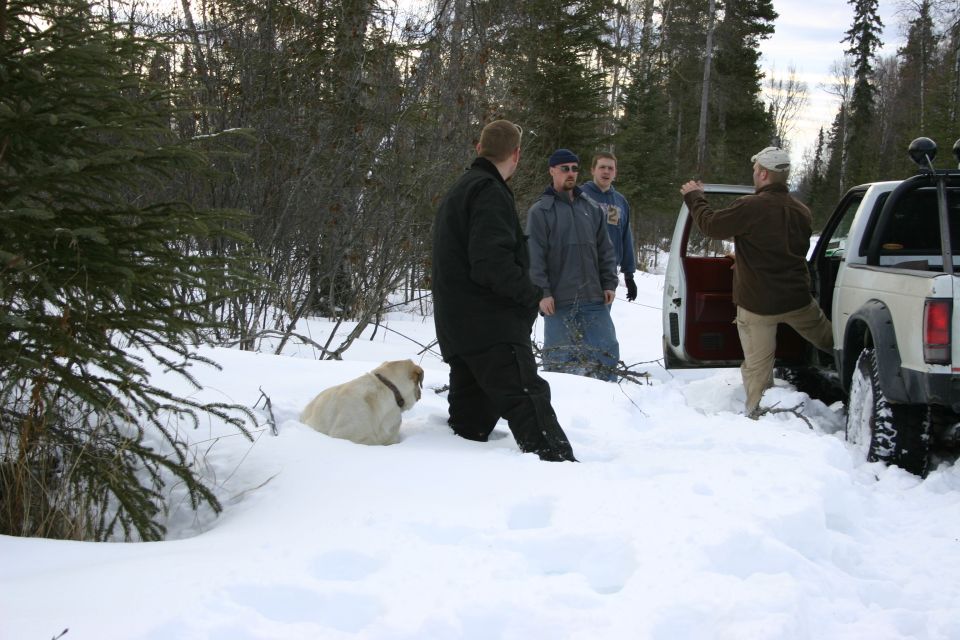 White pickup truck in snow with open door, people and dog nearby