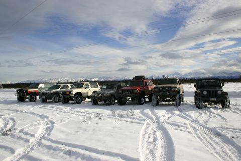 2003 Jeep TJ - A line of off-road vehicles are parked in a snow-covered landscape under a cloudy sky.