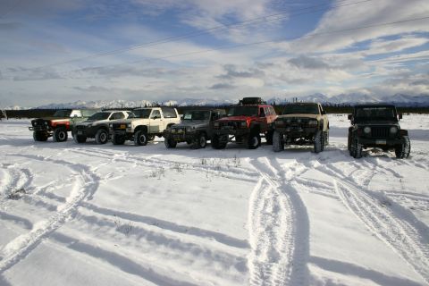 2003 Jeep TJ - A convoy of off-road vehicles is parked in a snow-covered landscape under a cloudy sky.