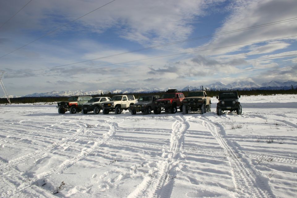 Several off-road vehicles parked in a snowy field with mountains in the background
