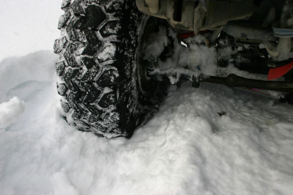 Close-up of a knobby off-road tire partially buried in snow, showing suspension components