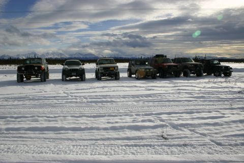 2003 Jeep TJ - A line of off-road vehicles sits parked in a snow-covered field under a cloudy sky.