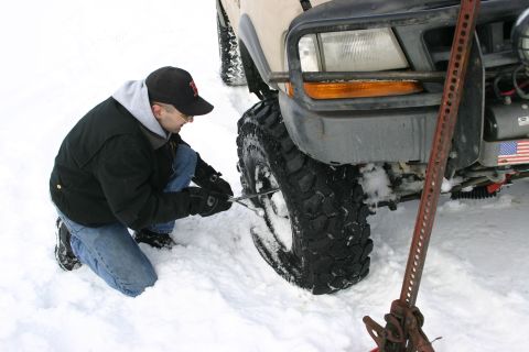2003 Jeep TJ - A man kneels in the snow to change a tire on a Jeep TJ.