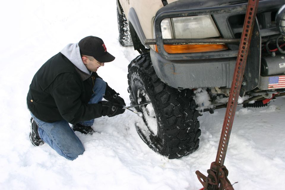 2003 Jeep TJ with large tires being changed by a man in the snow