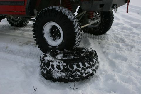 2003 Jeep TJ - A red Jeep TJ sits in the snow with one of its large off-road tires removed and placed on the ground.