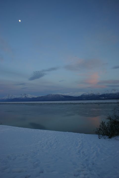 2003 Jeep TJ - A winter scene at dusk shows the moon in the sky above a body of water and distant snow-capped mountains.