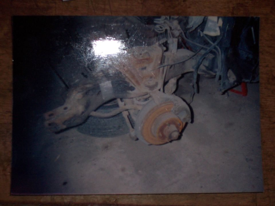 Printed photo of a car's front suspension and rusty brake rotor with the wheel removed