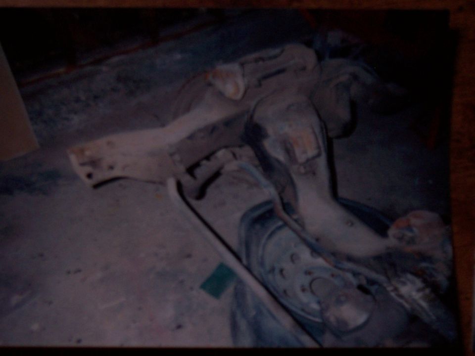 Bare front subframe with control arm lying on a dusty concrete shop floor