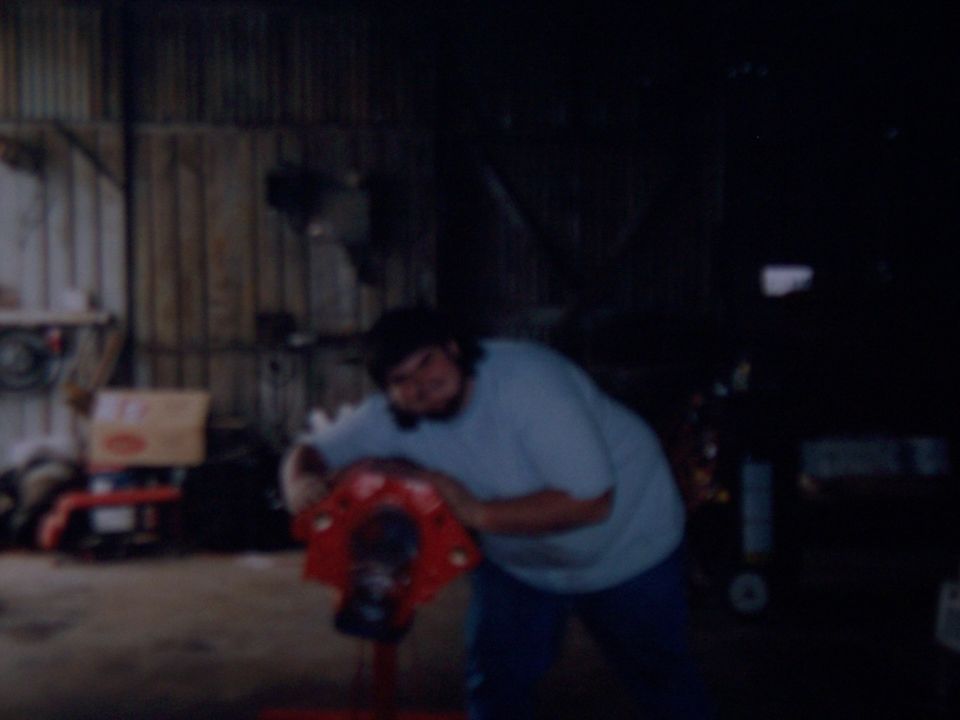 Person working on red-painted differential housing on a stand in a dim shop