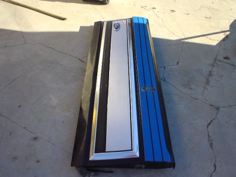 1993 Ford Bronco - A vehicle tailgate with a chrome trim and blue stripe accents is shown lying on a cracked concrete surface.