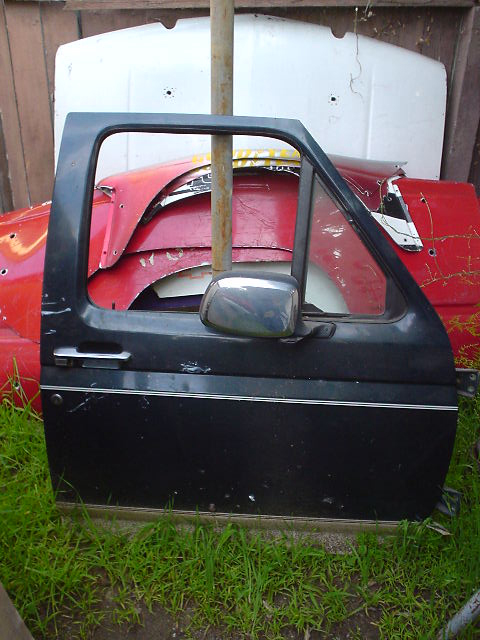 1993 Ford Bronco - A detached black car door is visible, with other vehicle parts stacked in the background.