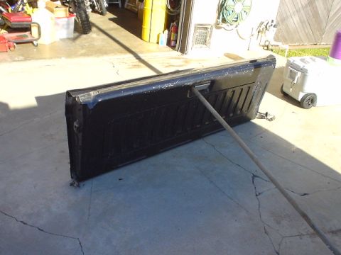 1993 Ford Bronco - A detached black tailgate rests on a cracked concrete surface, leaning against a support pole.