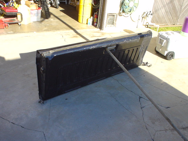 Black tailgate lying on concrete, propped open with a pole