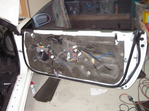 1994 Ford Probe - The interior of a car door is exposed, revealing its internal wiring and insulation. A red spray can rests on the floor nearby.