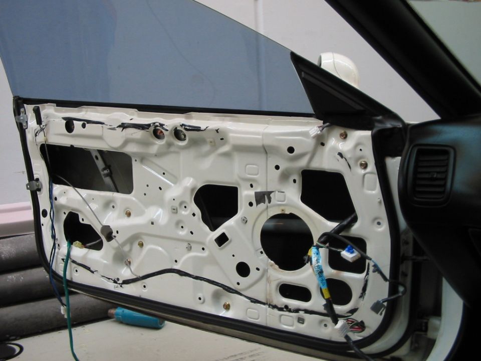 Car door with interior panel removed, showing wiring and internal structure. A blue object is on the floor