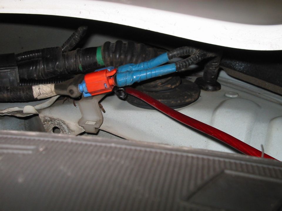 Close-up of automotive wiring harness with blue tape on connectors and a red wire