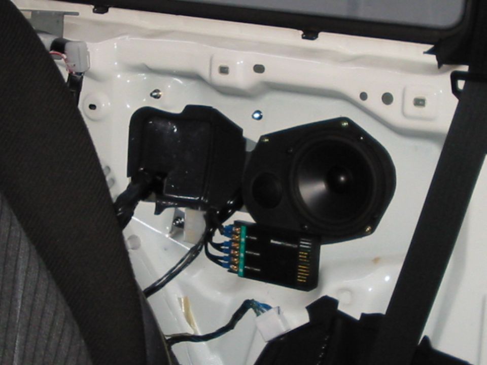 Car door interior showing speaker, black plastic housing, and wiring harness with green connector block