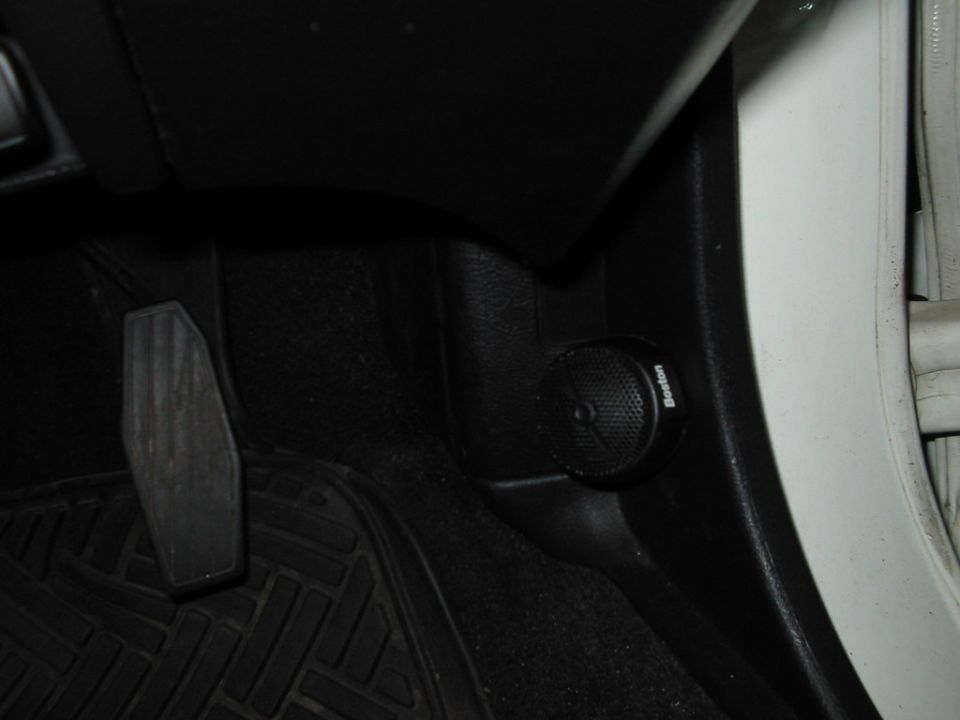 Car interior showing a black floor mat, gas pedal, and a small round speaker labeled 'Boston'