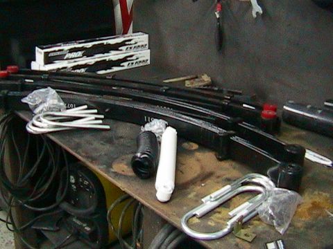 1981 Chevrolet C/K Pickup - Parts laid out on a workbench, including leaf springs, U-bolts, and shock absorbers, with boxes of 'PRO' parts visible.