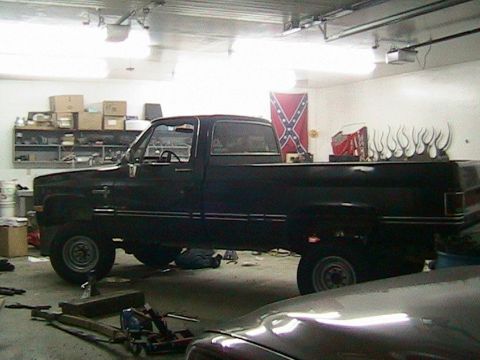 1981 Chevrolet C/K Pickup - A black pickup truck is parked in a garage, with a Confederate flag visible in the background.