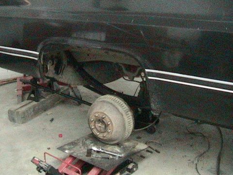 1981 Chevrolet C/K Pickup - The rear suspension and axle of a vehicle are visible, supported by jack stands and blocks, with tools scattered around.