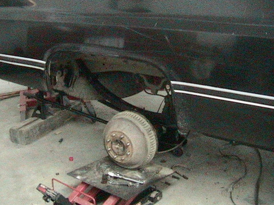 rear axle and drum brake assembly of a vehicle on jack stands, with tools on the floor