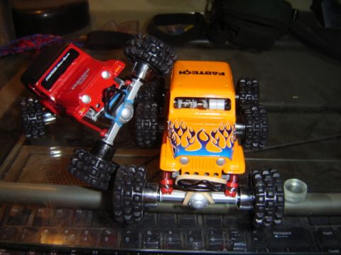 1992 Ford Bronco - Two remote control toy trucks are positioned on a keyboard, one orange with flames and the other red.