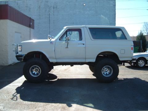 1989 Ford Bronco - A lifted white Ford Bronco is parked on asphalt with another vehicle visible to the right.