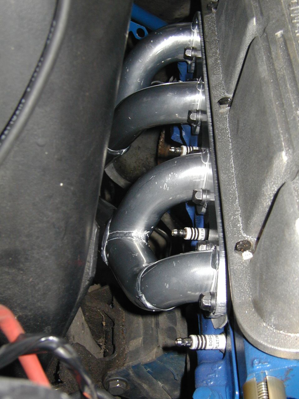 Close-up of shiny metal exhaust headers bolted to an engine block, with spark plugs visible