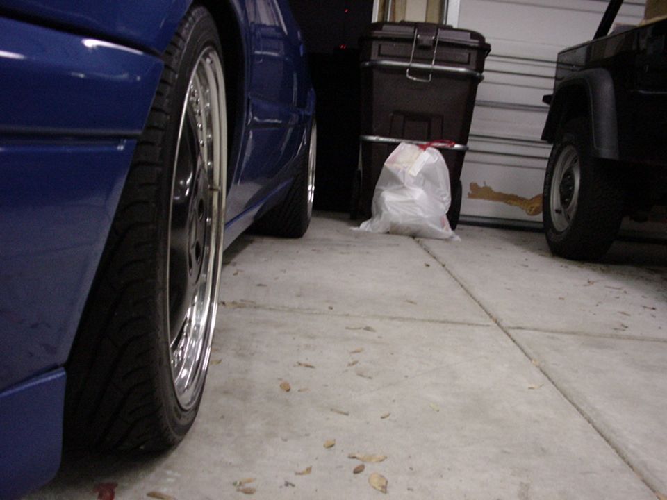 Blue sedan's rear wheel and side panel, next to a black Jeep in a garage
