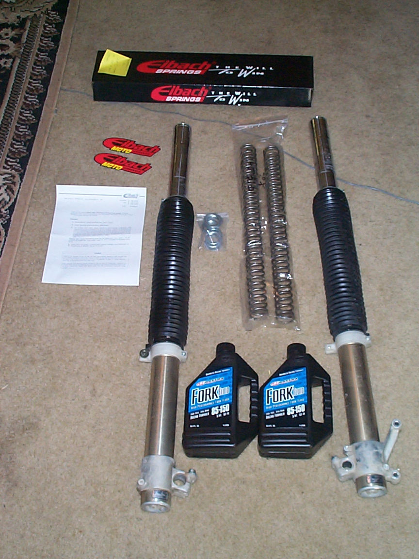Two motorcycle fork legs, Eibach fork springs, box, instructions, and two bottles of Maxima 85-150 fork oil on carpet